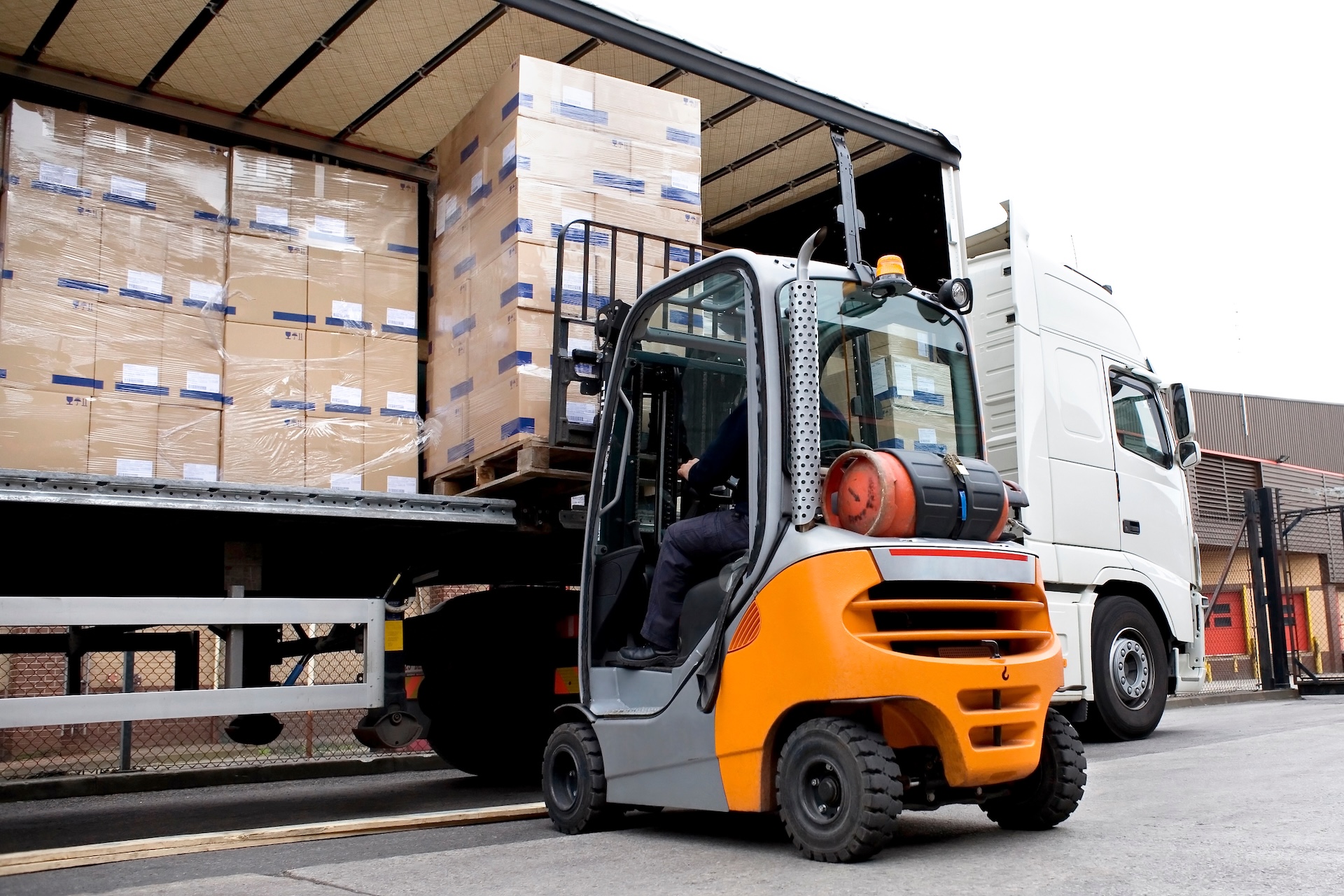 A forklift loading pallets of boxes onto a curtain-sided lorry