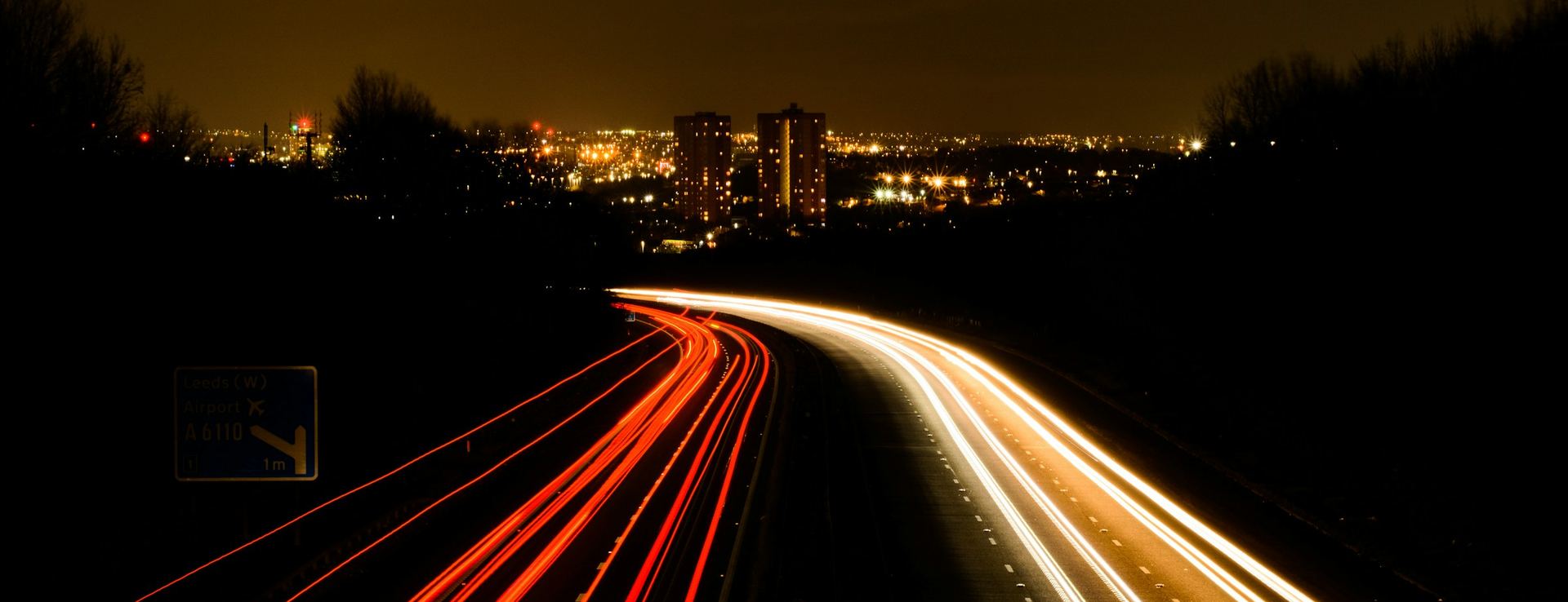 A motorway at night, with the lights of the traffic drawn out into lines